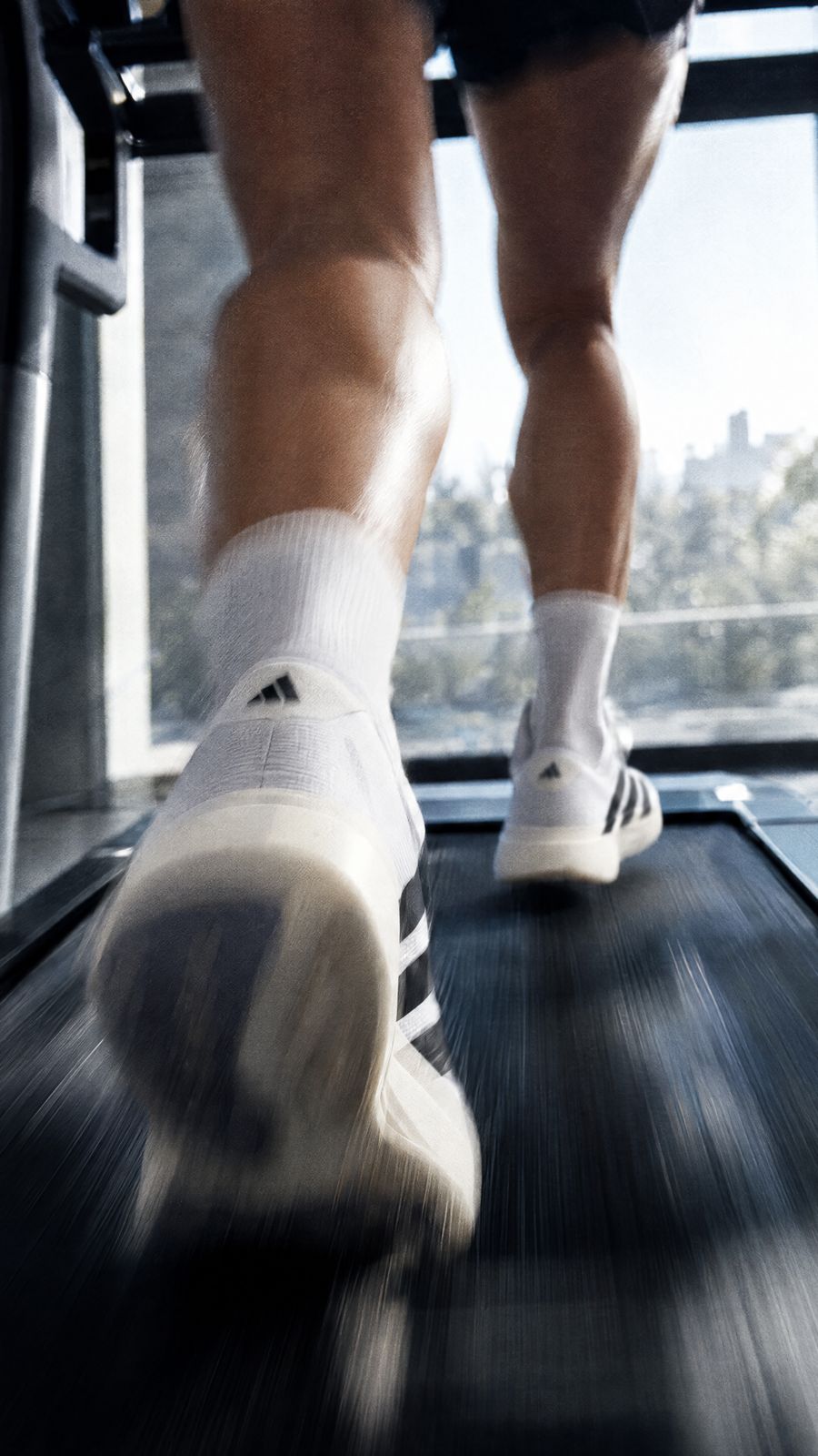 White running shoes blurred mid stride on a treadmill belt, a bright window behind.