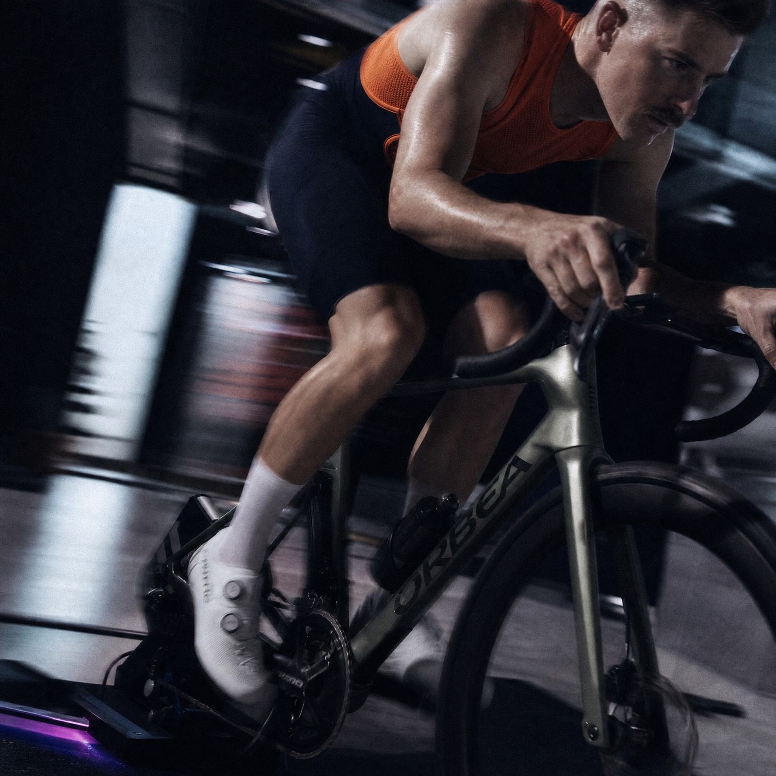 A rider out of the saddle on an indoor trainer, legs blurred with effort.